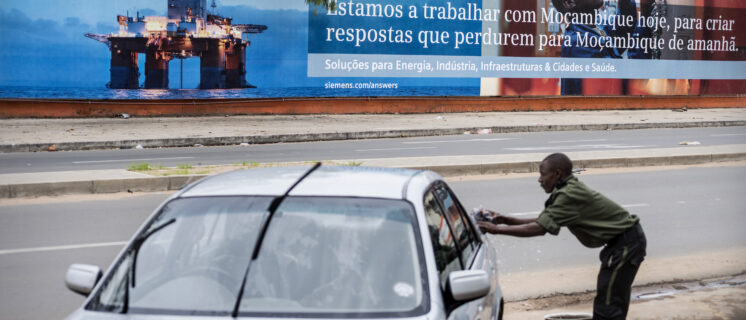 A man washes a car with a billboard showing an off-shore oil rig with the sign written in Portuguese in Maputo. Mozambique's economy is one of the fastest growing due to foreign investment and the discovery of natural reserves.